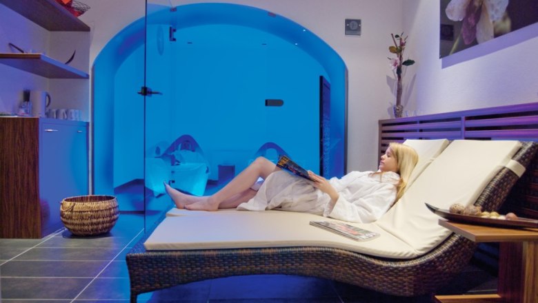 Woman relaxing on a lounger in the wellness area with blue lighting.