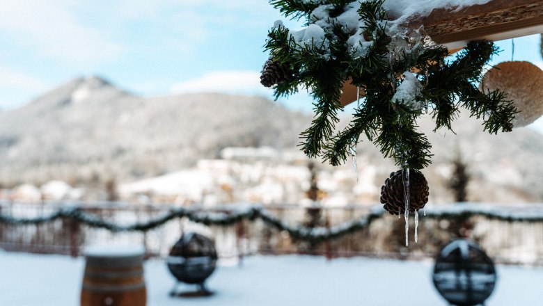 Winter terrace with fir branches and icicles in the foreground, snow-covered landscape in the background.