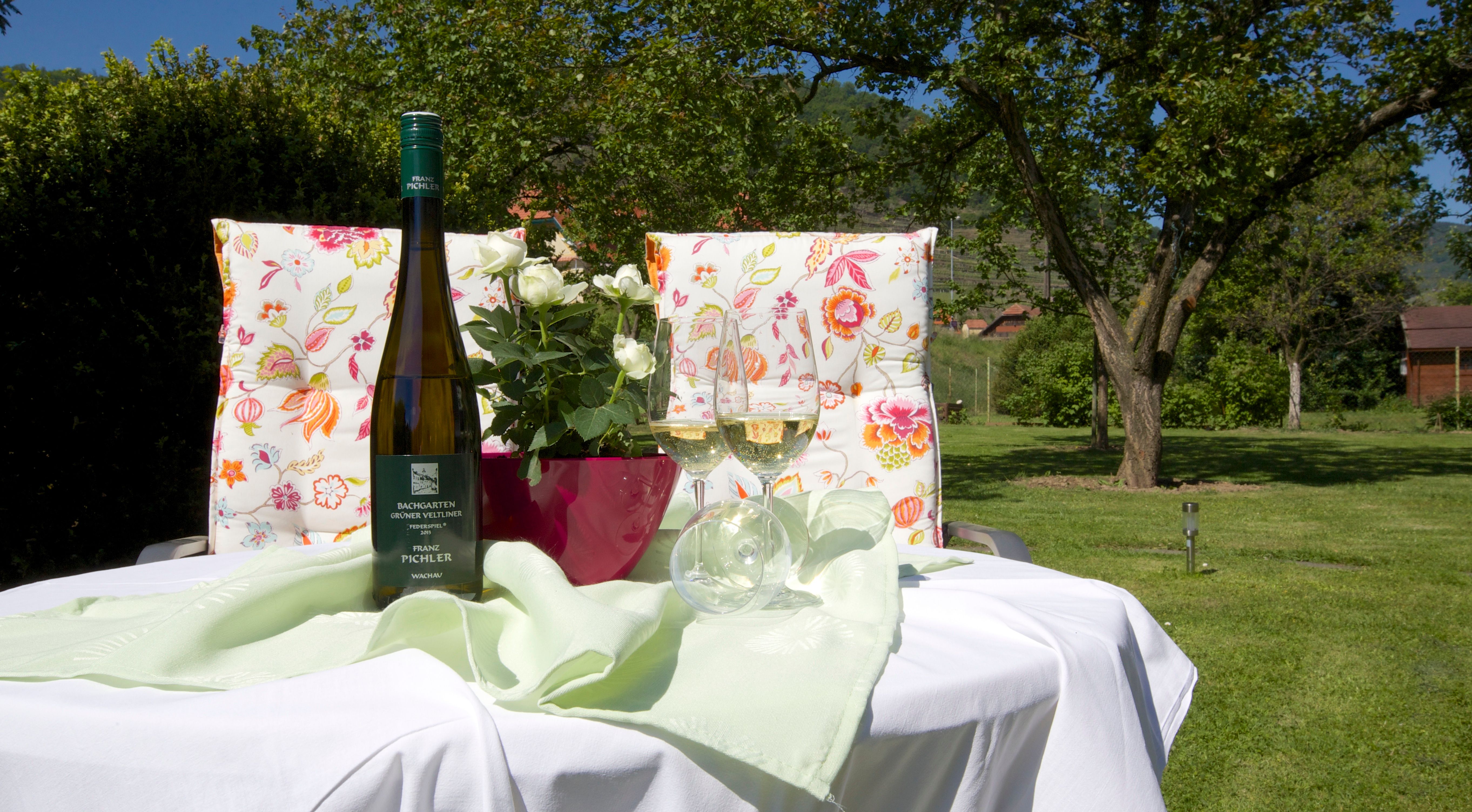 A table in the garden with a bottle of wine, two glasses and a bouquet of flowers.