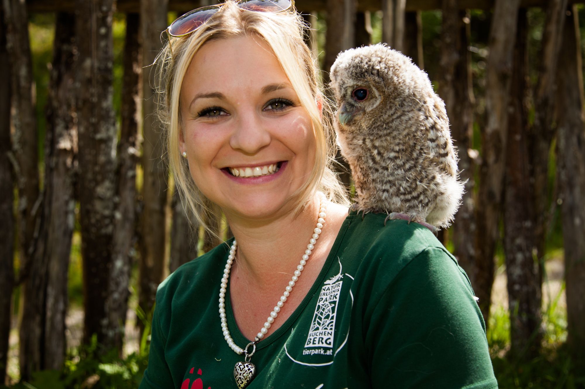 A woman laughs into the camera while an owl sits quietly on her shoulder.