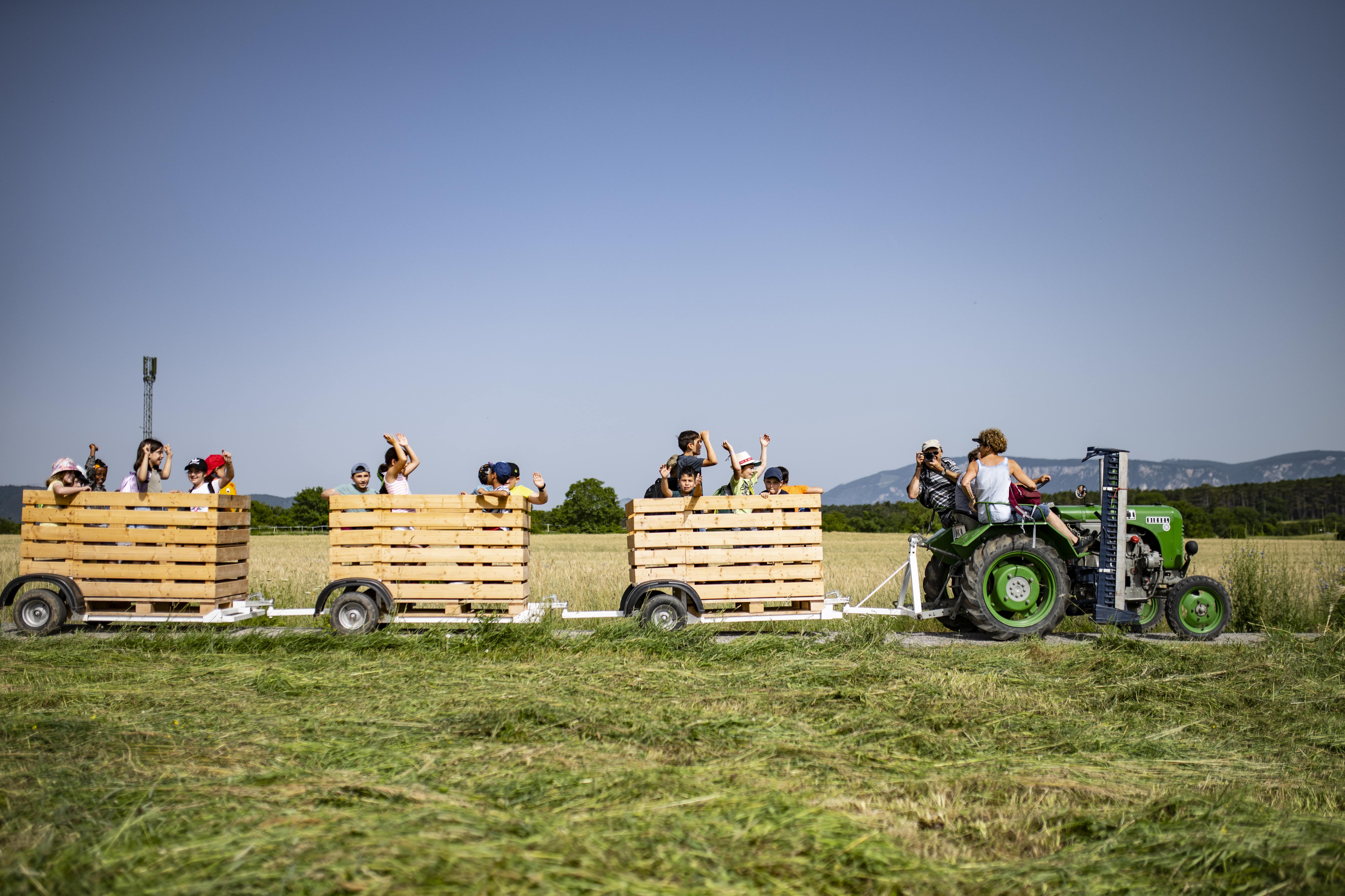 A tractor pulls a trailer full of happy people through a field.