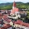Aerial view of a village with a church and vineyards in the background.