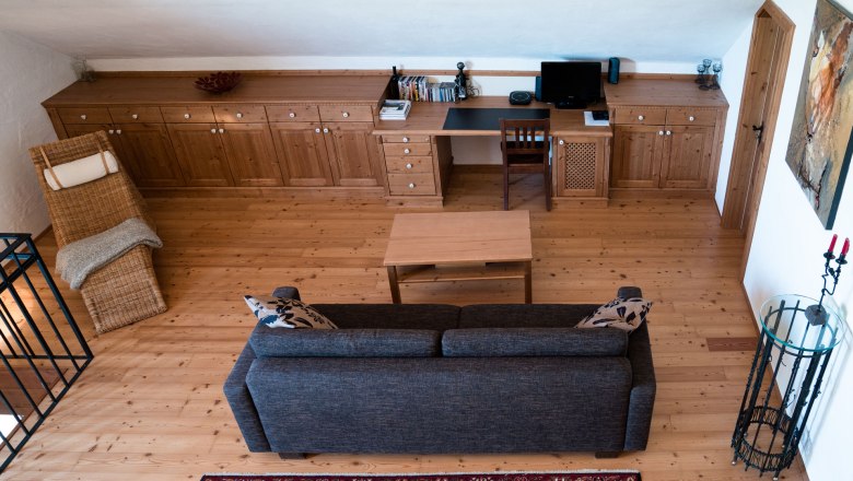 Living room on the upper floor with wooden floor, sofa, table, desk and chair.