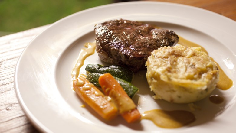 A plate with a piece of meat, vegetables and a potato side dish.