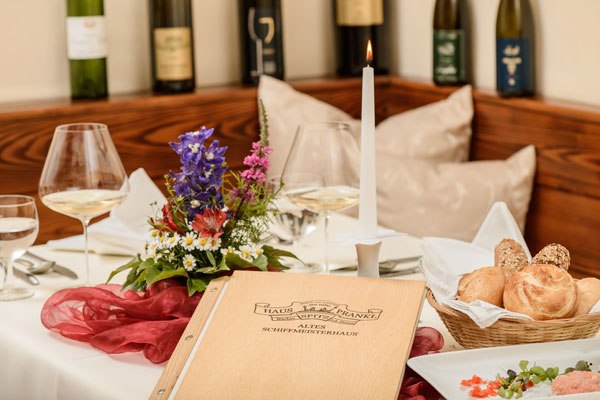Elegant table setting with menu, candle, flowers and bottles of wine in the background.