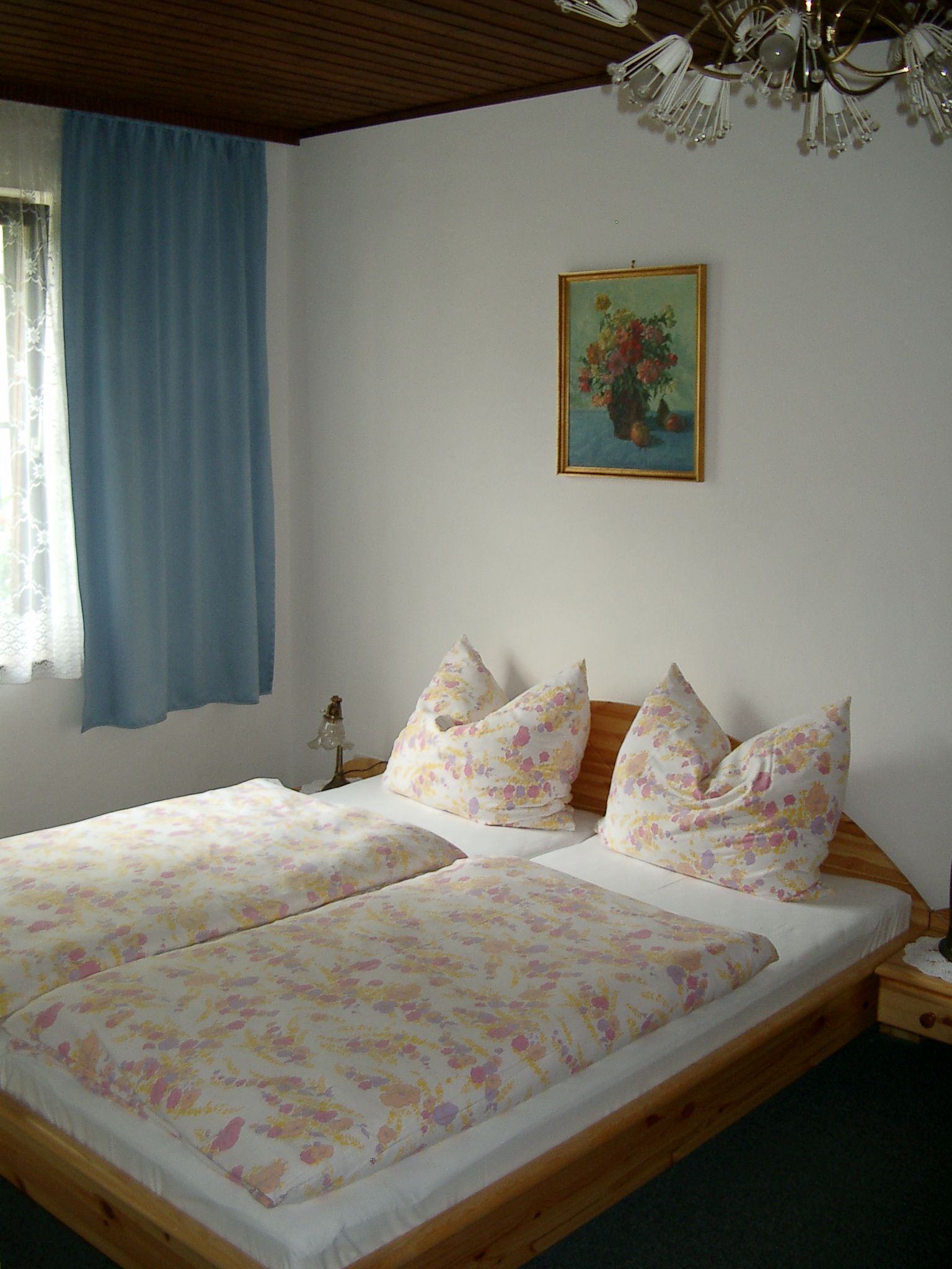 Bedroom with double bed, blue curtains and flower picture on the wall.
