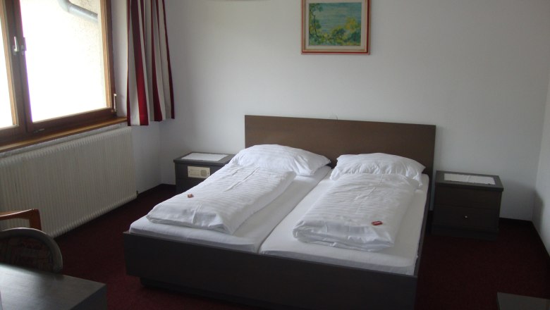 A simply furnished hotel room with a double bed, bedside tables and a window with curtains.