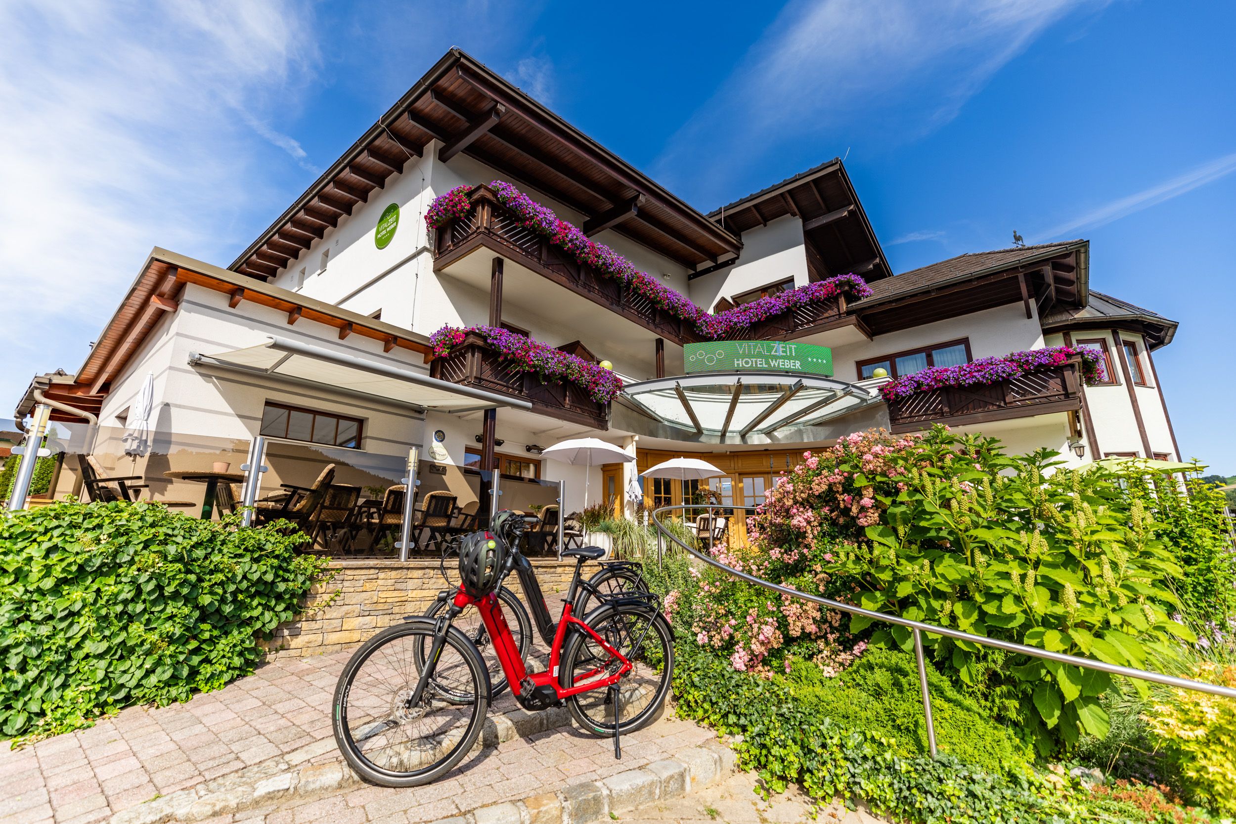 Exterior view of the Vitalzeit Hotel Weber with flowers and bicycle.