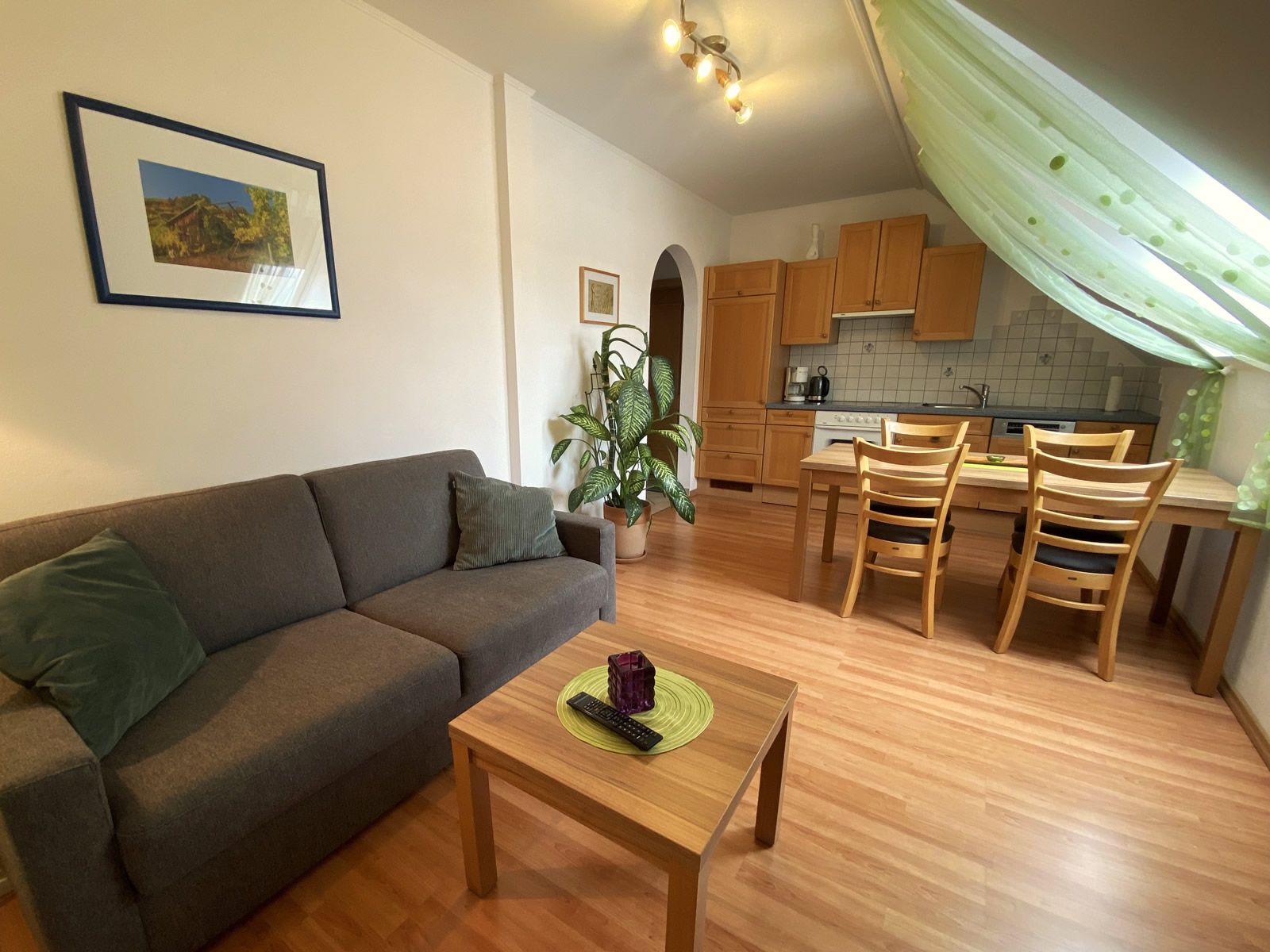 Living room with gray sofa, wooden table, dining table and kitchen in the background.