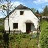 Small white cottage with garden and trees, surrounded by green countryside.