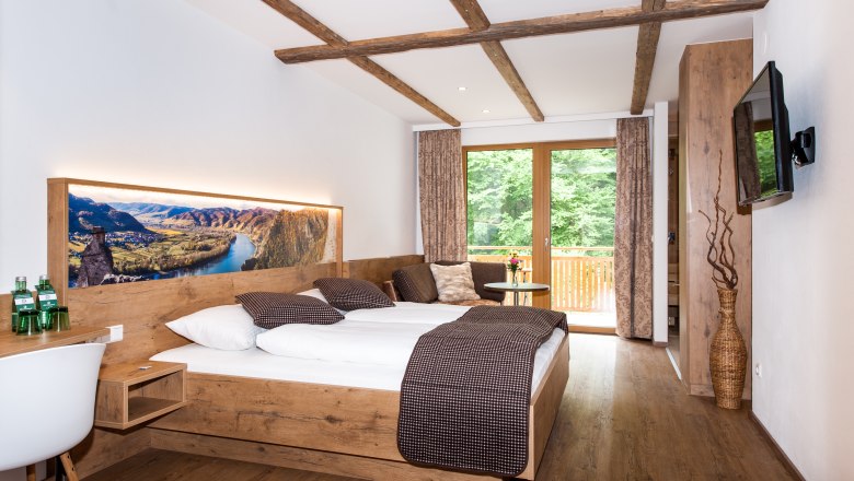 Modern hotel room with wooden furniture, large bed and balcony with a view of the countryside.
