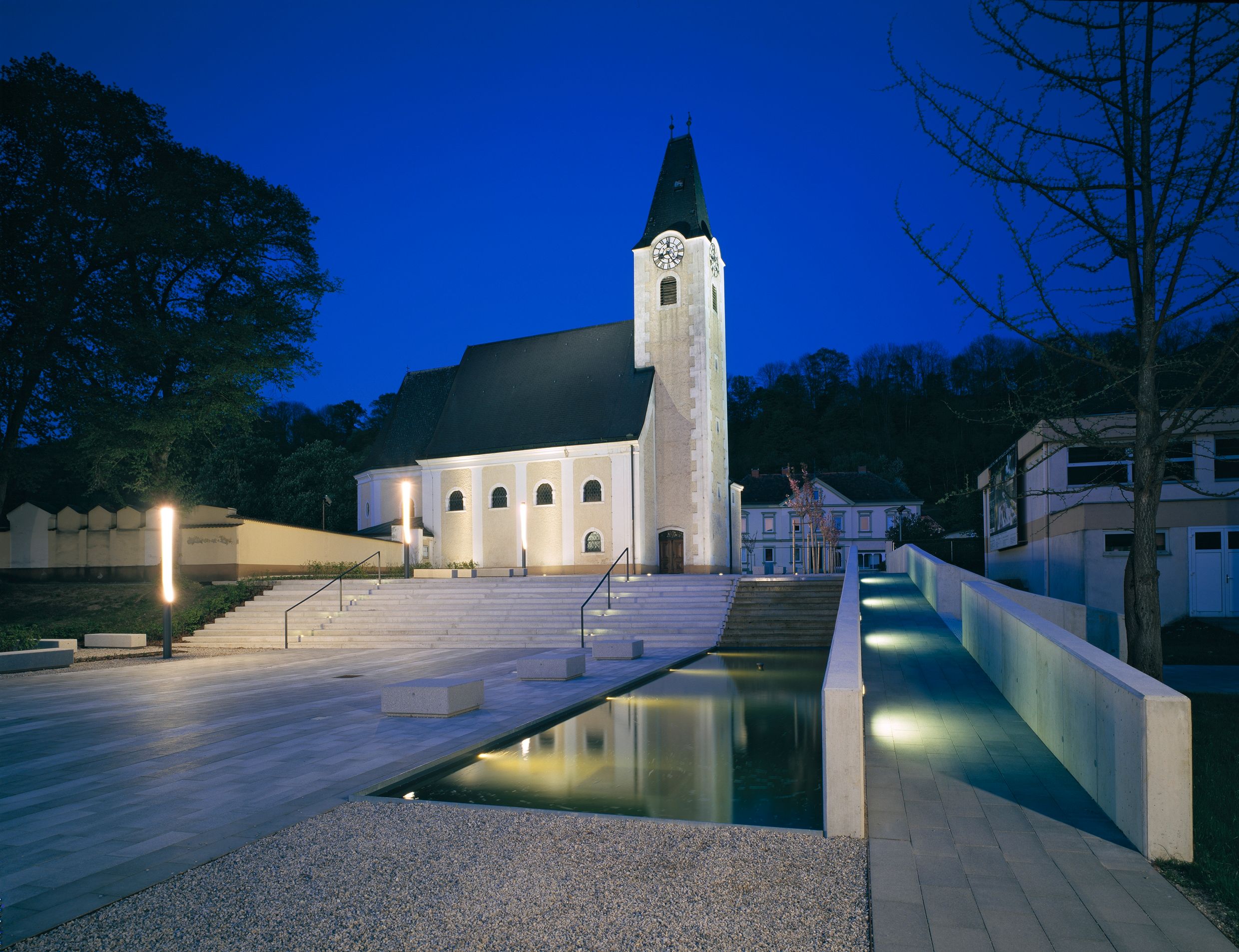 Evening shot of an illuminated church square with steps and water basin in Ernsthofen.