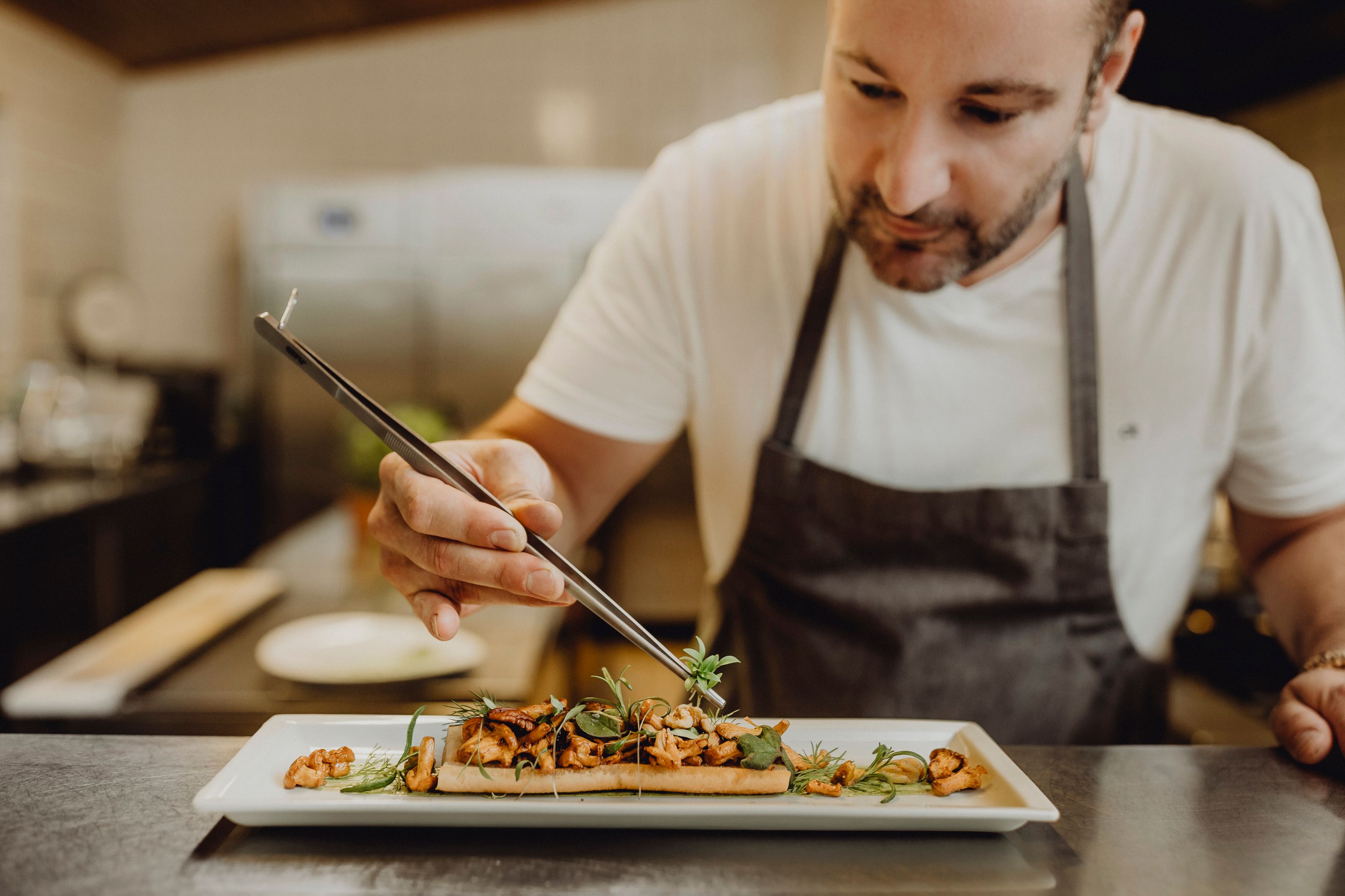 A chef arranges a dish on a plate with a pair of tweezers.