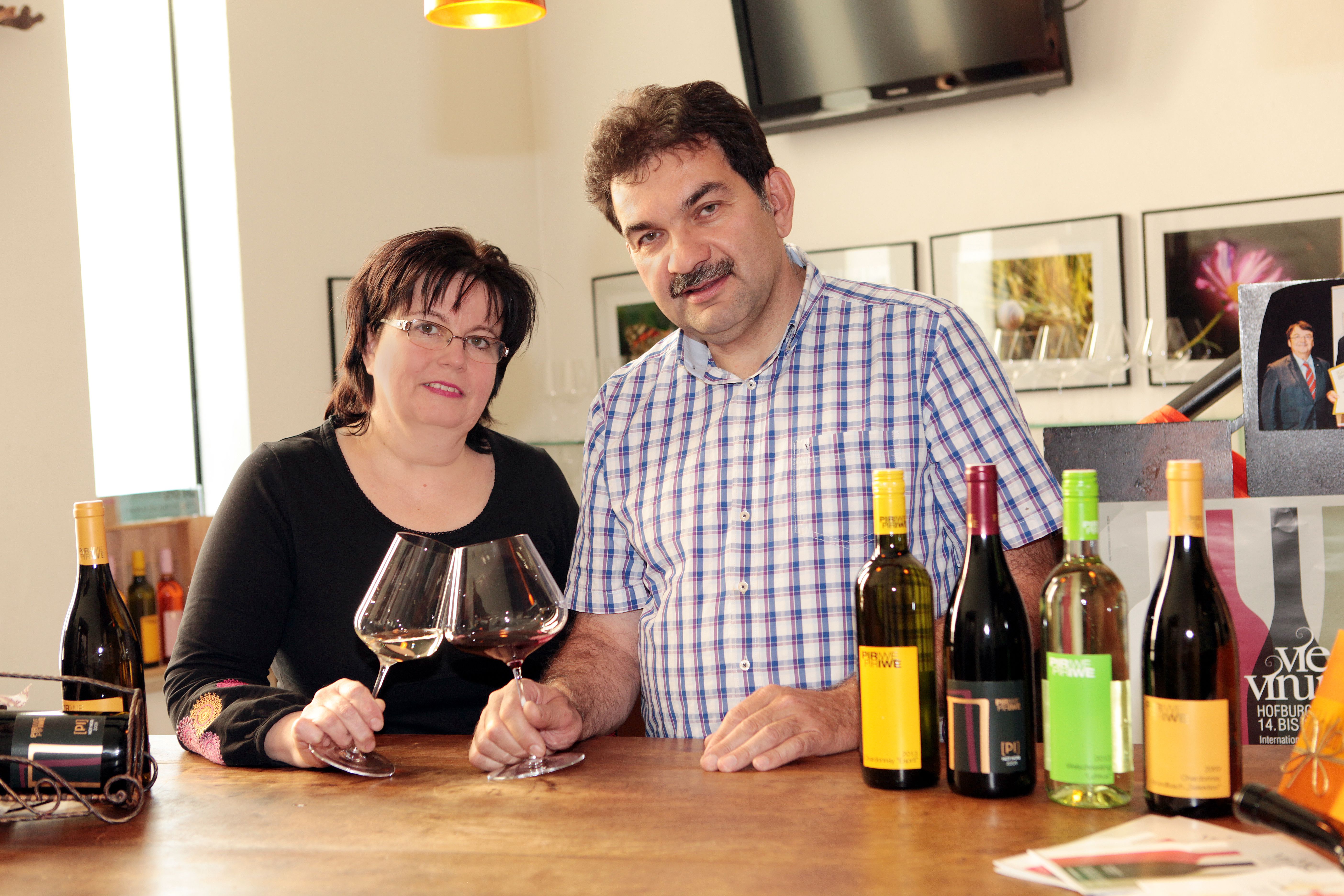 A man and a woman are standing at a table with wine glasses and bottles of wine.