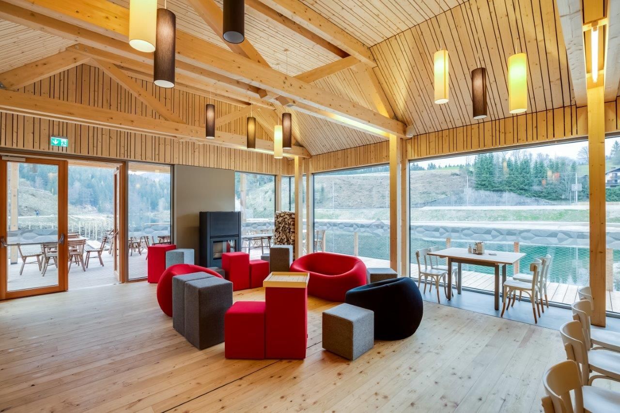 Interior view of a modern room with wooden walls, colorful seating and large windows overlooking a terrace and nature.