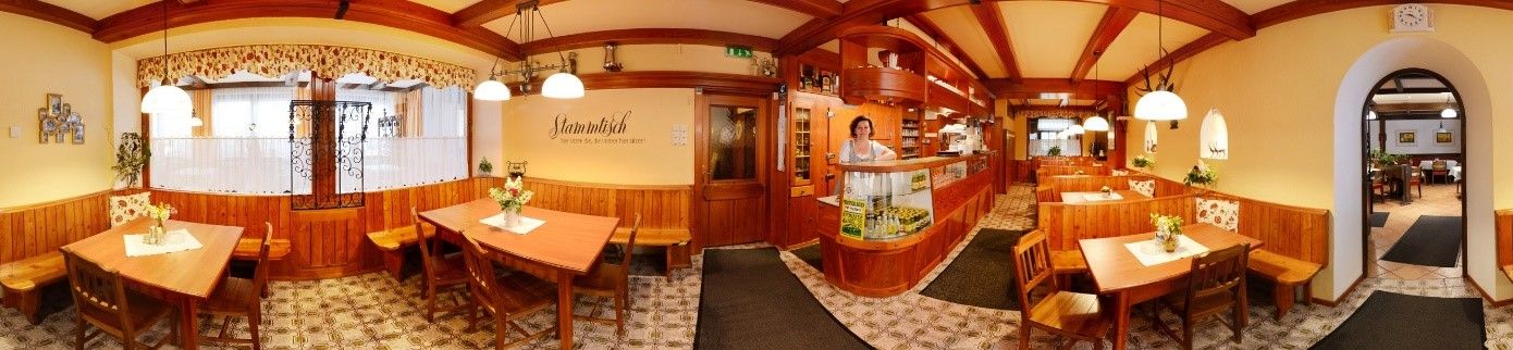 Panorama of a cozy restaurant with wooden furniture and decorative lamps.