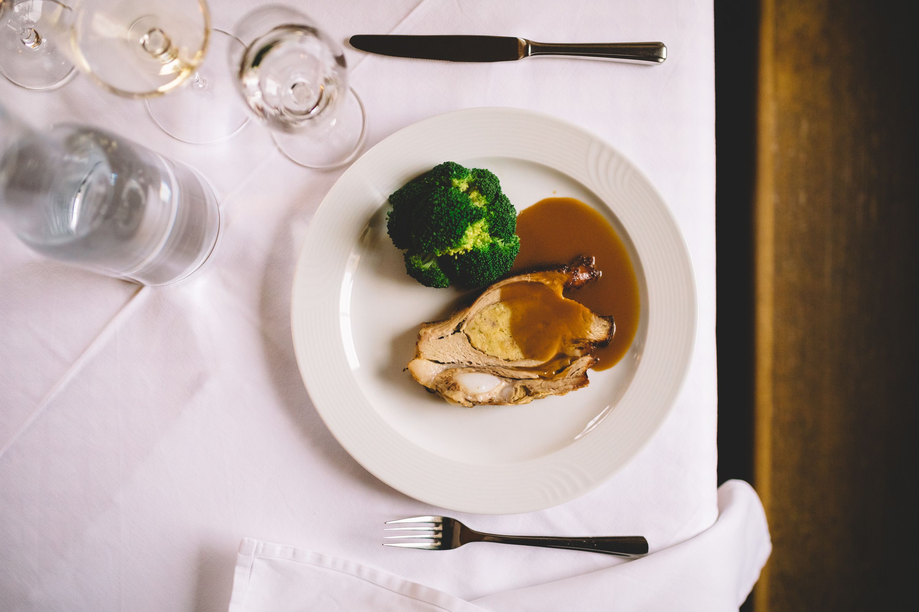 Stuffed veal breast with broccoli and sauce on a white plate.