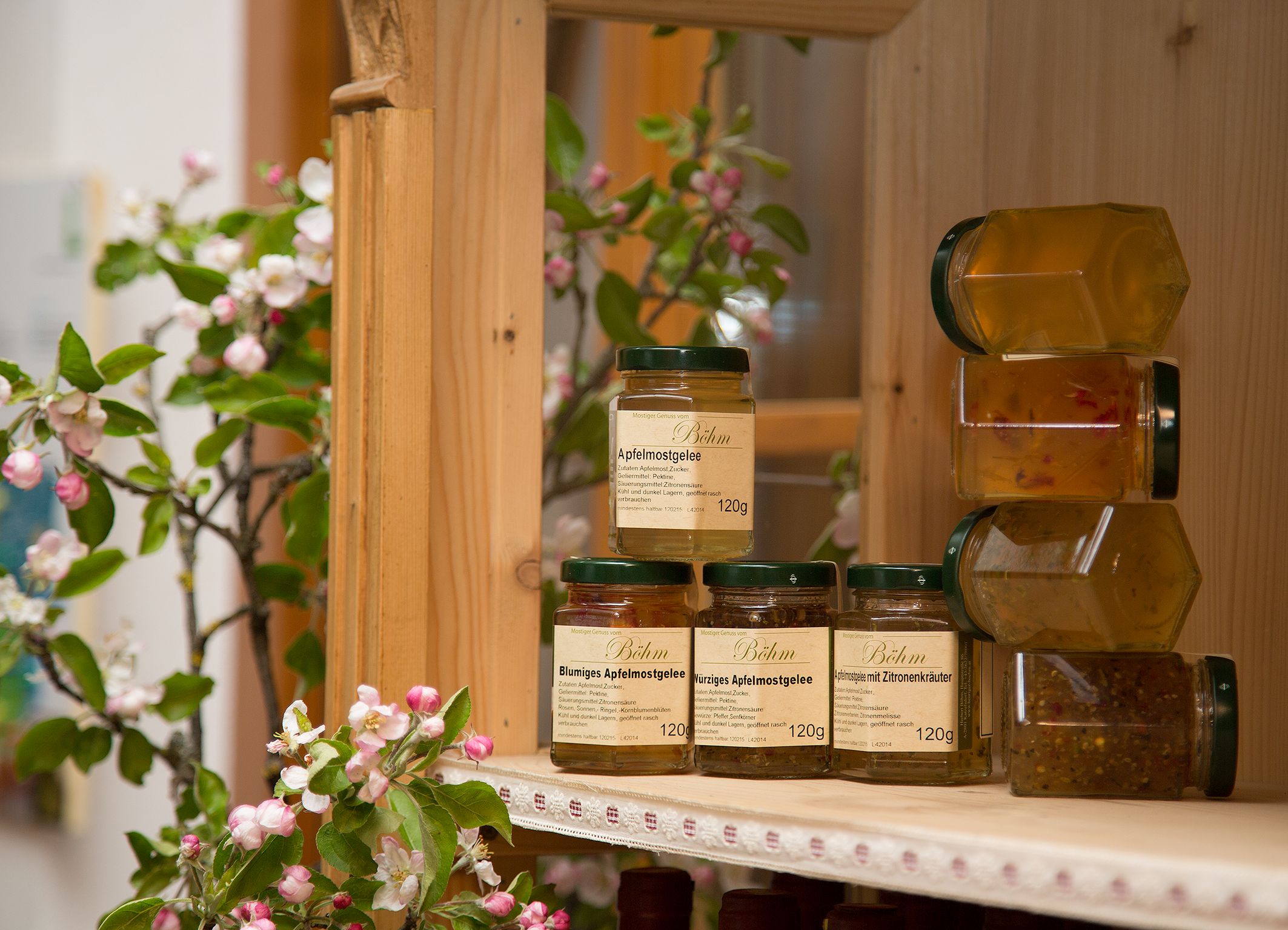 Jars of apple cider jelly on a wooden shelf, surrounded by blossoming apple branches.