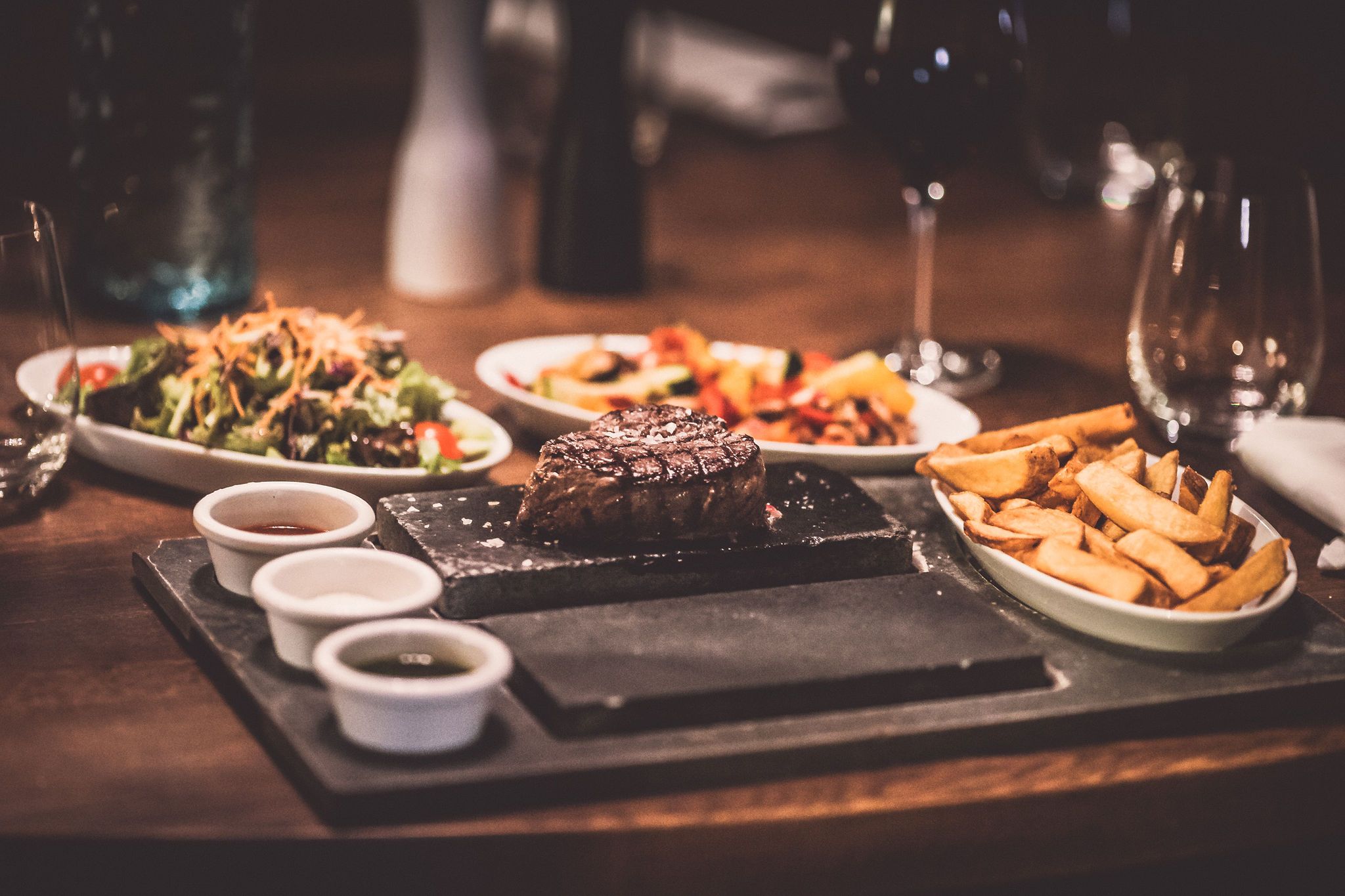 A plate with steak and chips, salad and sauces on a table next to it.