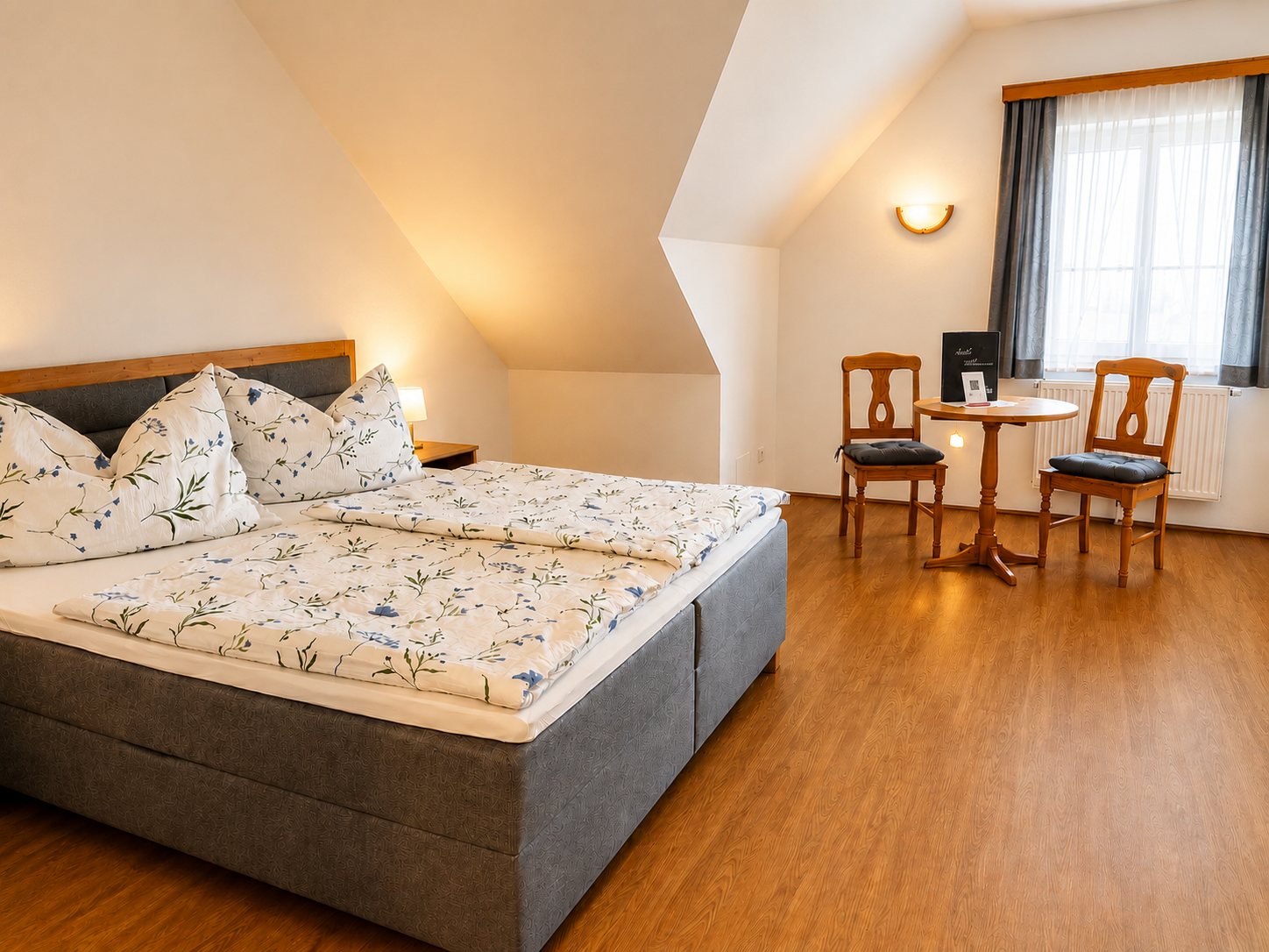 Cozy bedroom with double bed, wooden floor and small table with two chairs.