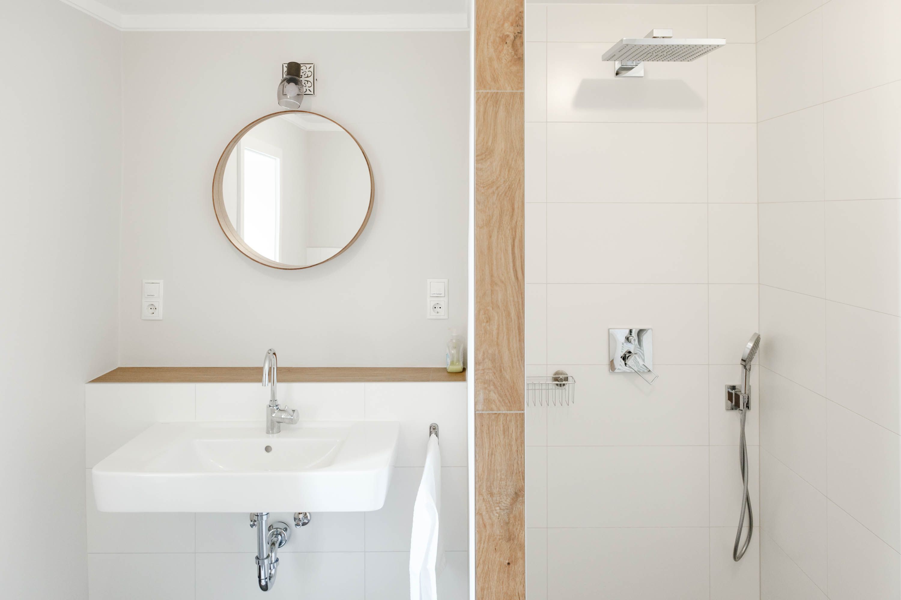 Modern bathroom with round mirror, washbasin and shower.