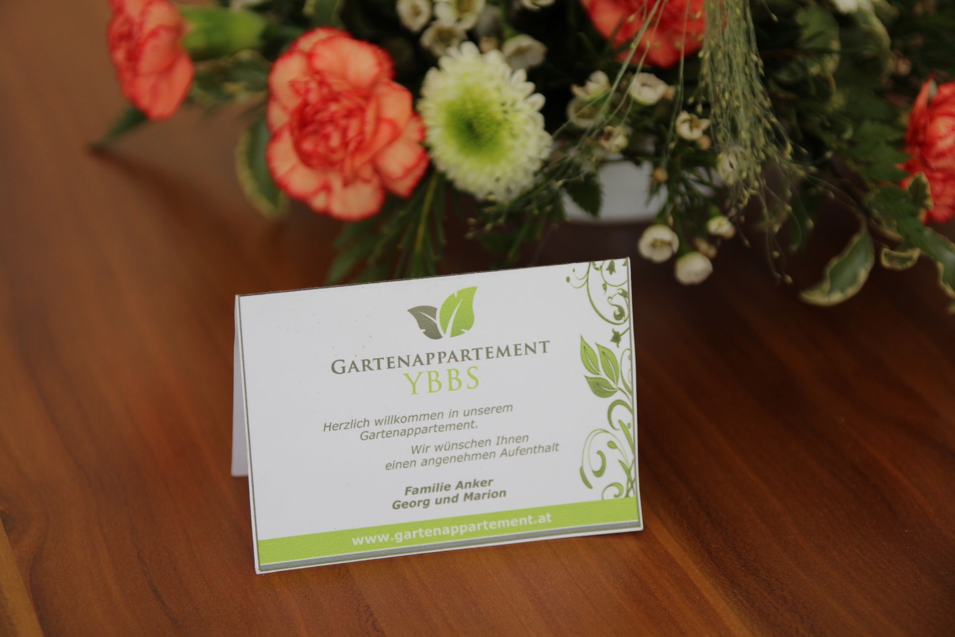 Welcome card of the Gartenappartement Ybbs on a table with flowers.