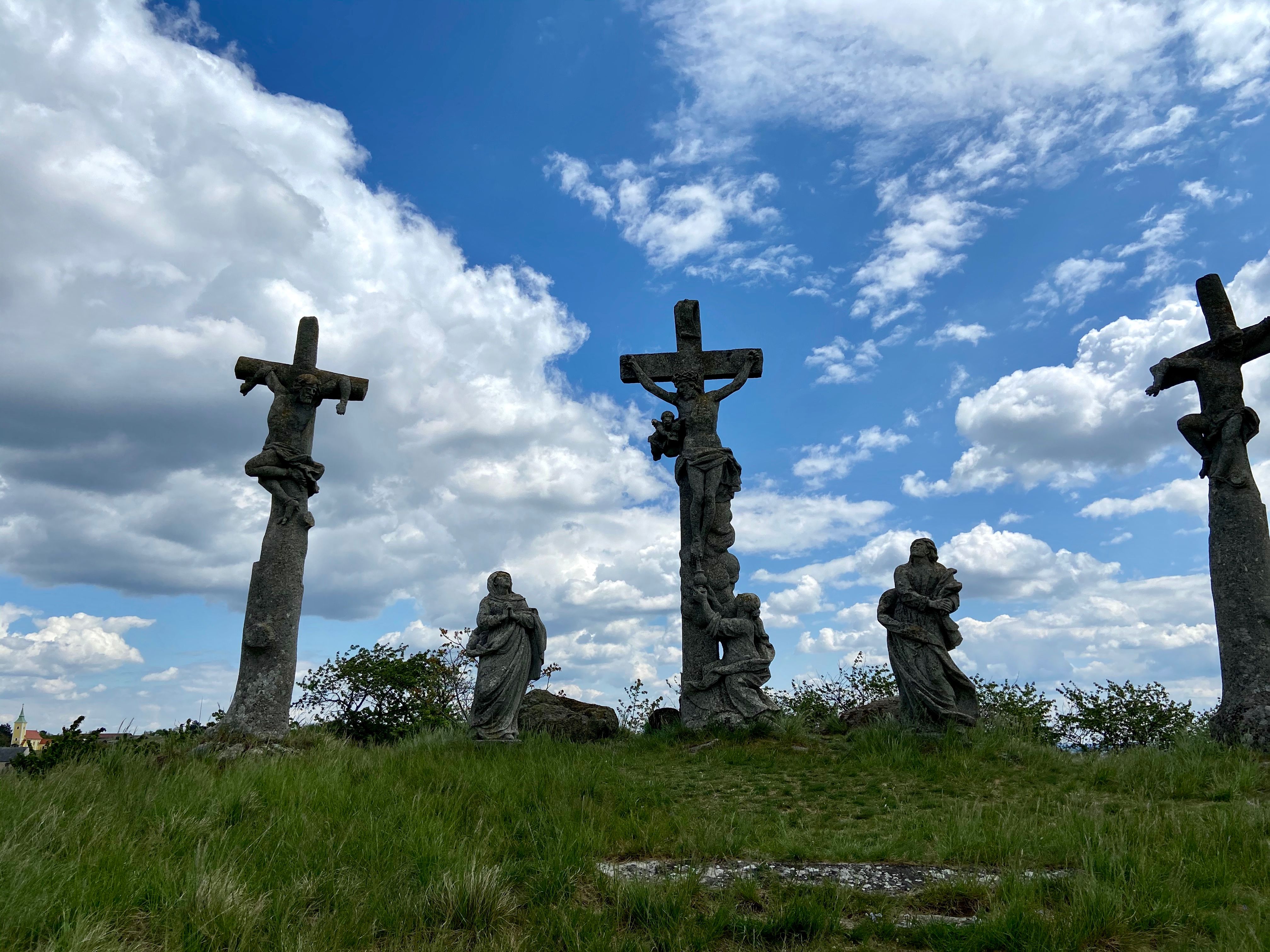 Three stone crosses with figures on a hill under a cloudy sky.