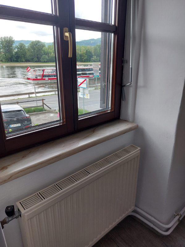 View from a window onto a river with a passing boat and a parked car.