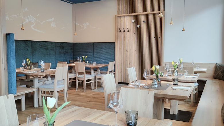 Modern restaurant with wooden furniture, laid tables, ceiling lamps and blue accents.