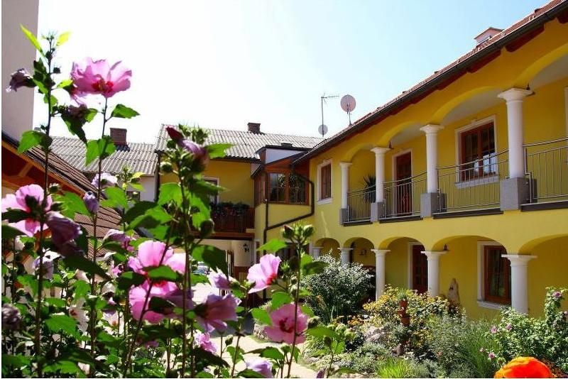 A sunny courtyard with a yellow building, white columns and blooming pink flowers in the foreground.