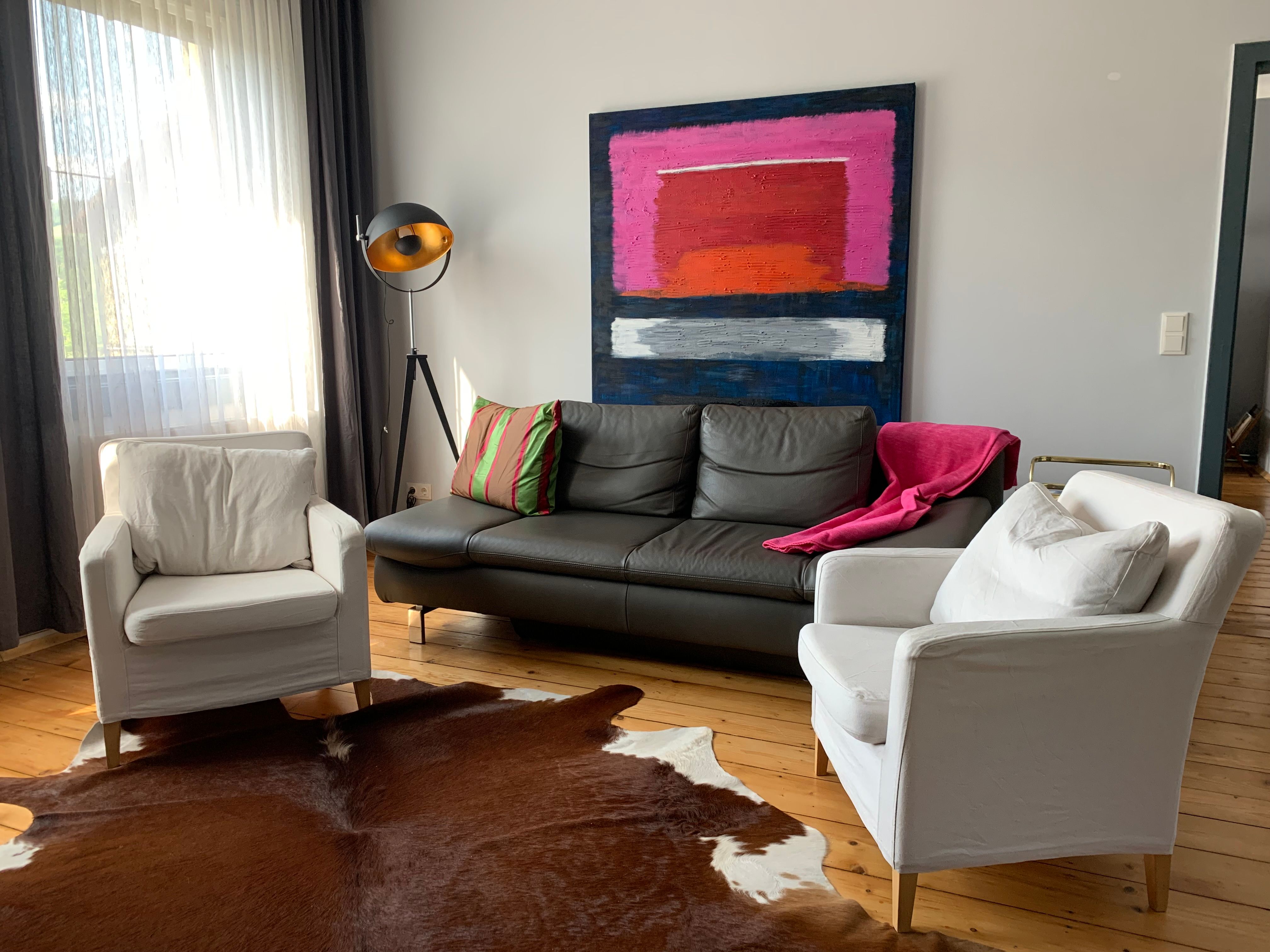 Modern living room with leather sofa, two white armchairs, floor lamp and abstract painting on the wall.