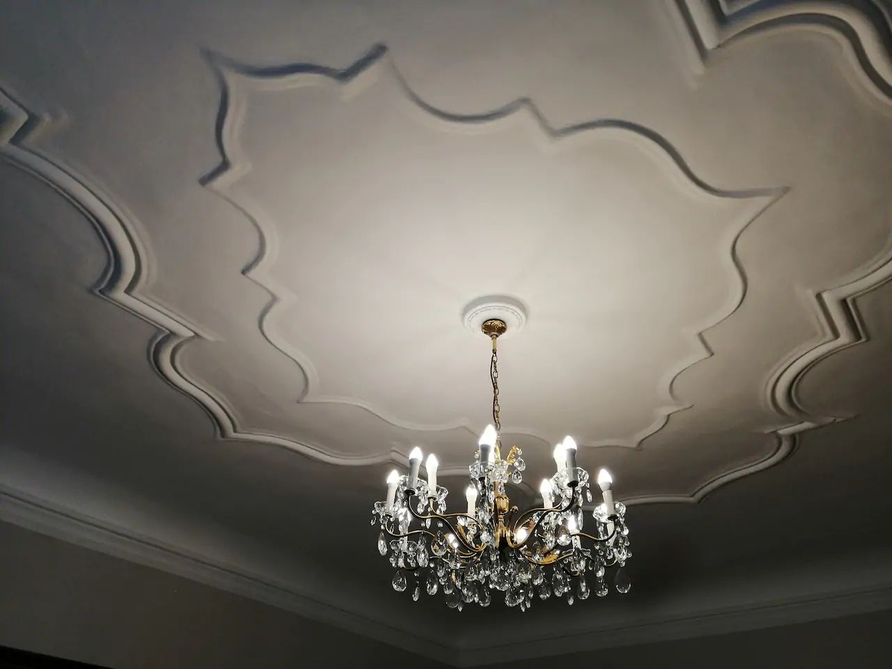 A chandelier hangs from a decorative ceiling with stucco decorations.