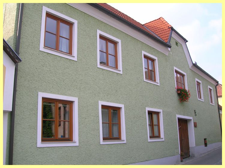 Green house with red roof tiles and wooden windows.