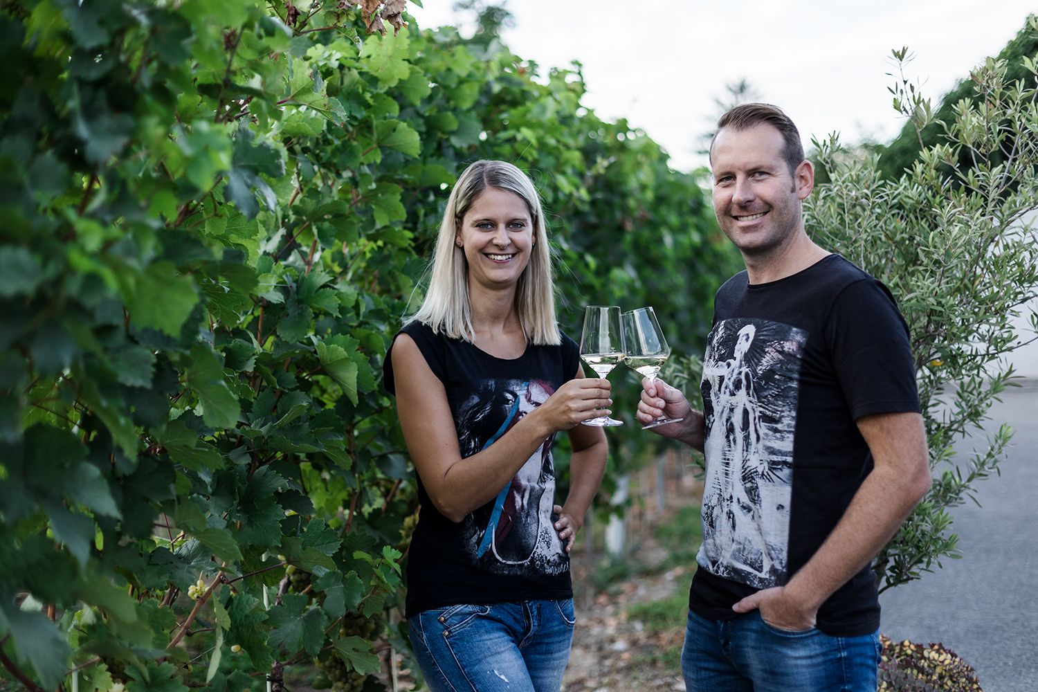 Two people clink glasses in a vineyard.