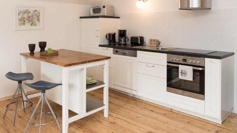 Modern kitchen with white furnishings, wooden floor and small dining table with two stools.