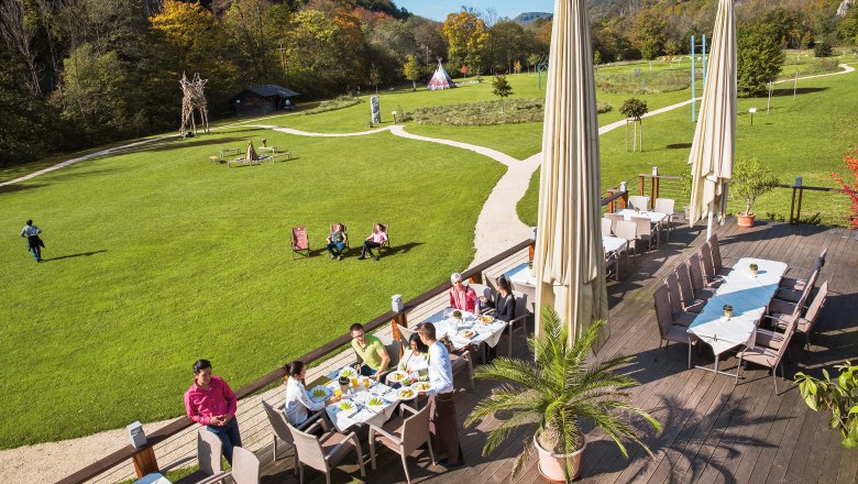 Terrace of the seminar and event hotel Krainerhütte with guests eating, surrounded by green meadows and forest.