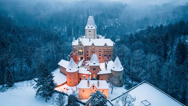 Aerial view of Ottenstein Castle in winter, surrounded by snow-covered trees and an illuminated courtyard.
