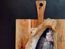 A fish wrapped in paper on a wooden board.
