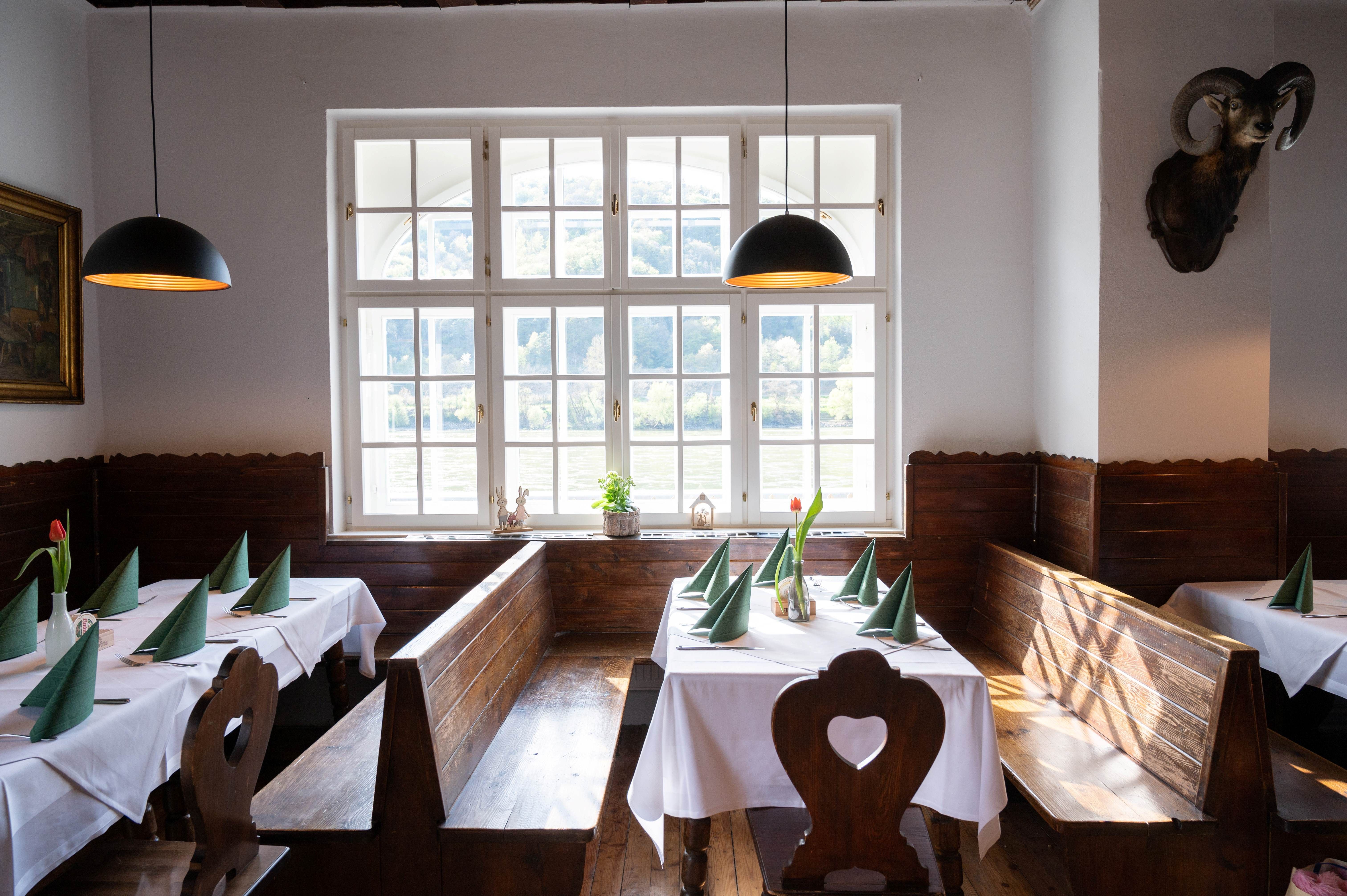 Cozy dining room with wooden benches, white tablecloths and green napkins. Large windows with a view of nature.