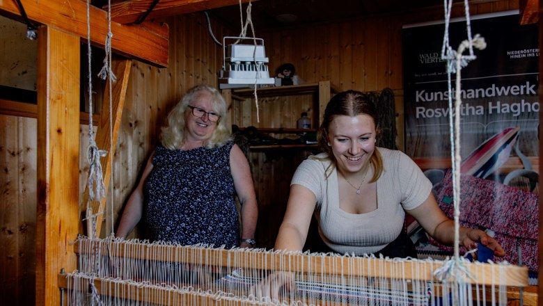 Two women work at a loom in a workshop.