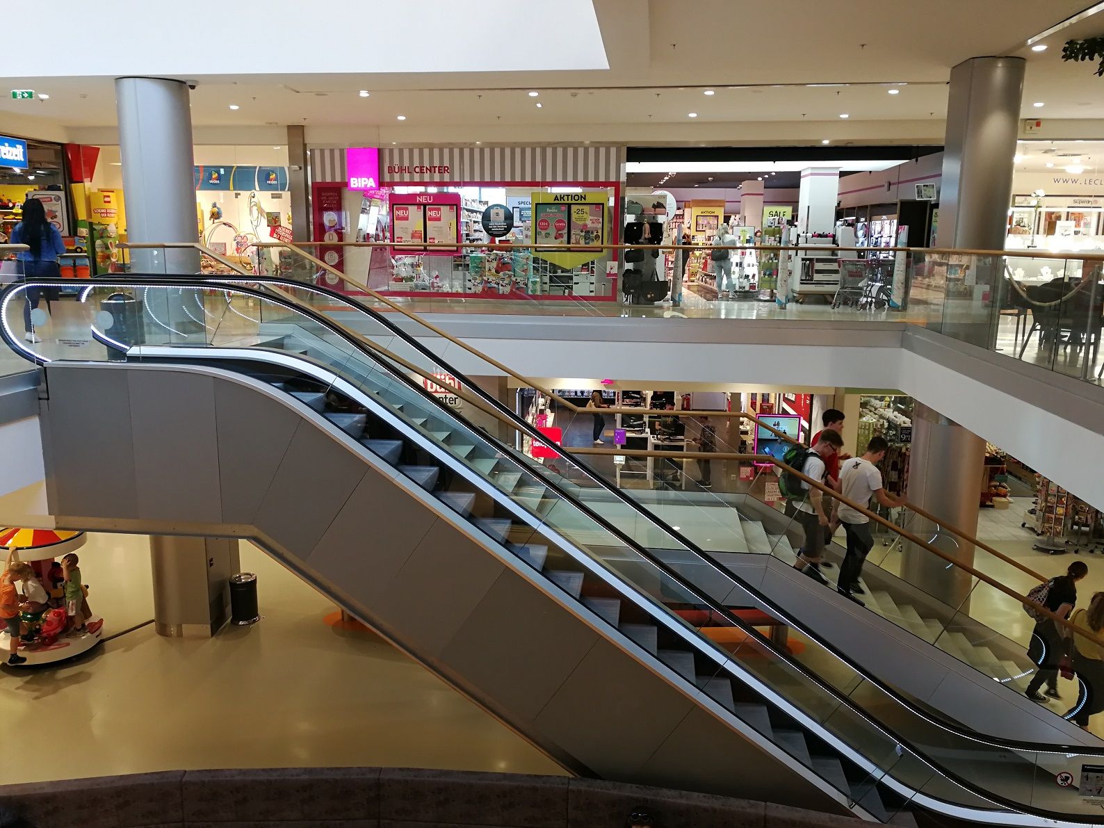 Interior view of a shopping center with escalators and stores.