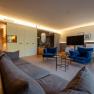 Modern hotel room with blue armchairs, gray sofa, large bed and stylish lighting.
