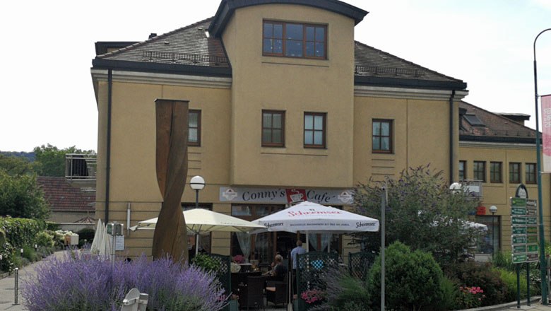 Exterior view of Conny's Café in Gars with parasols and plants.