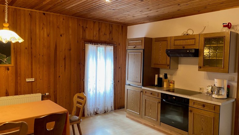 Rustic kitchen with wooden walls, dining table and chairs, as well as modern kitchenette with appliances.