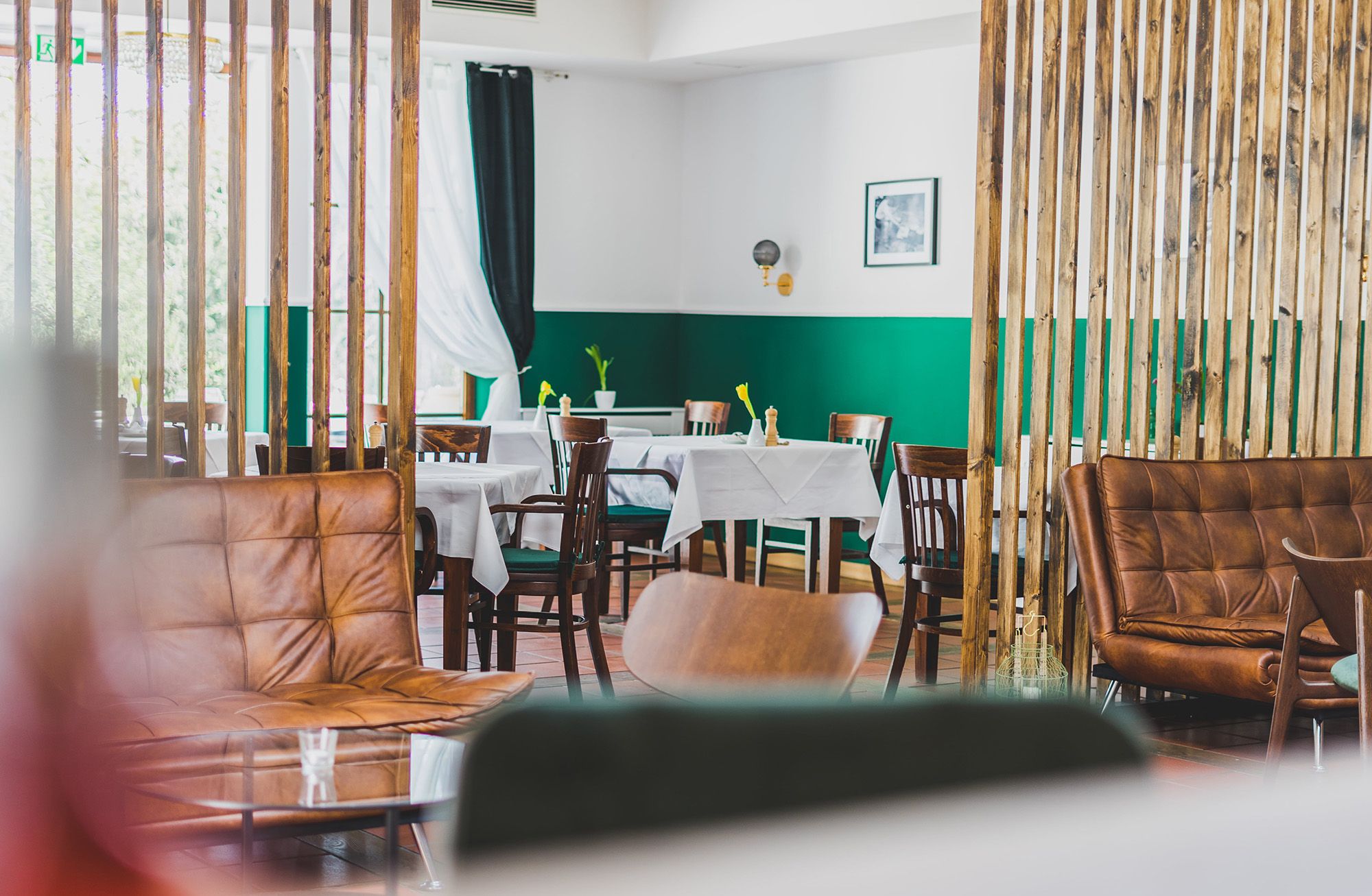 A stylishly furnished dining room with wooden furniture, green walls and white tablecloths.