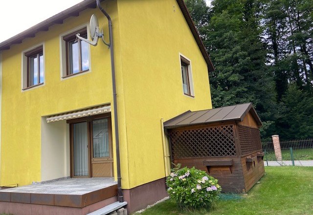 Yellow vacation home with terrace and small annex surrounded by trees.