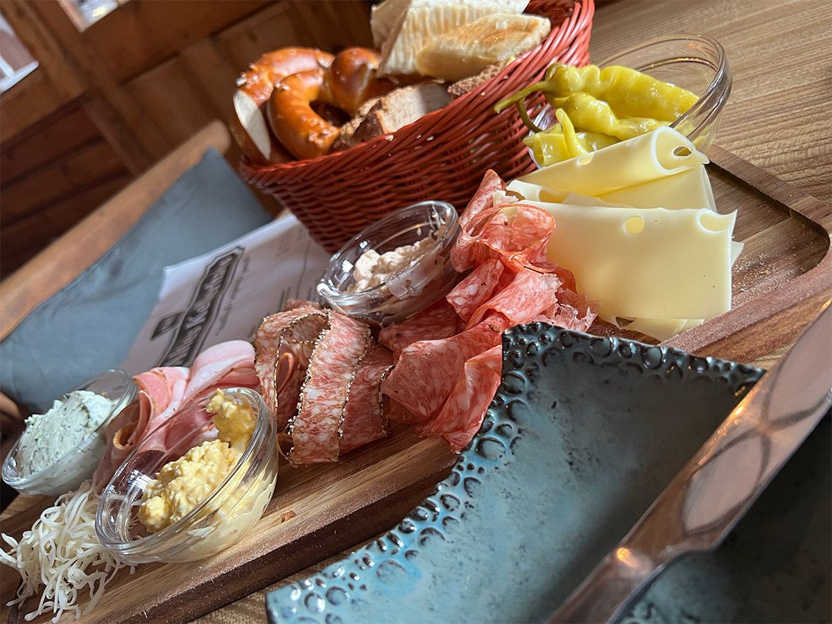 A rustic snack with sausage, cheese, bread and spreads on a wooden plate.