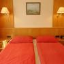 Guest room with two single beds, red comforters, wooden furniture and wall lamps.