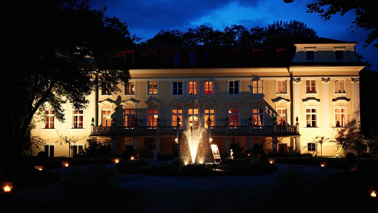 Illuminated Stuppach Castle at night with a fountain in the foreground.