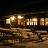 Snow-covered benches in front of an illuminated hut at night.